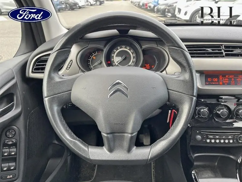 Vue rapprochée du volant Citroën C3 2014 avec tableau de bord et commandes noires, affichage digital orange.