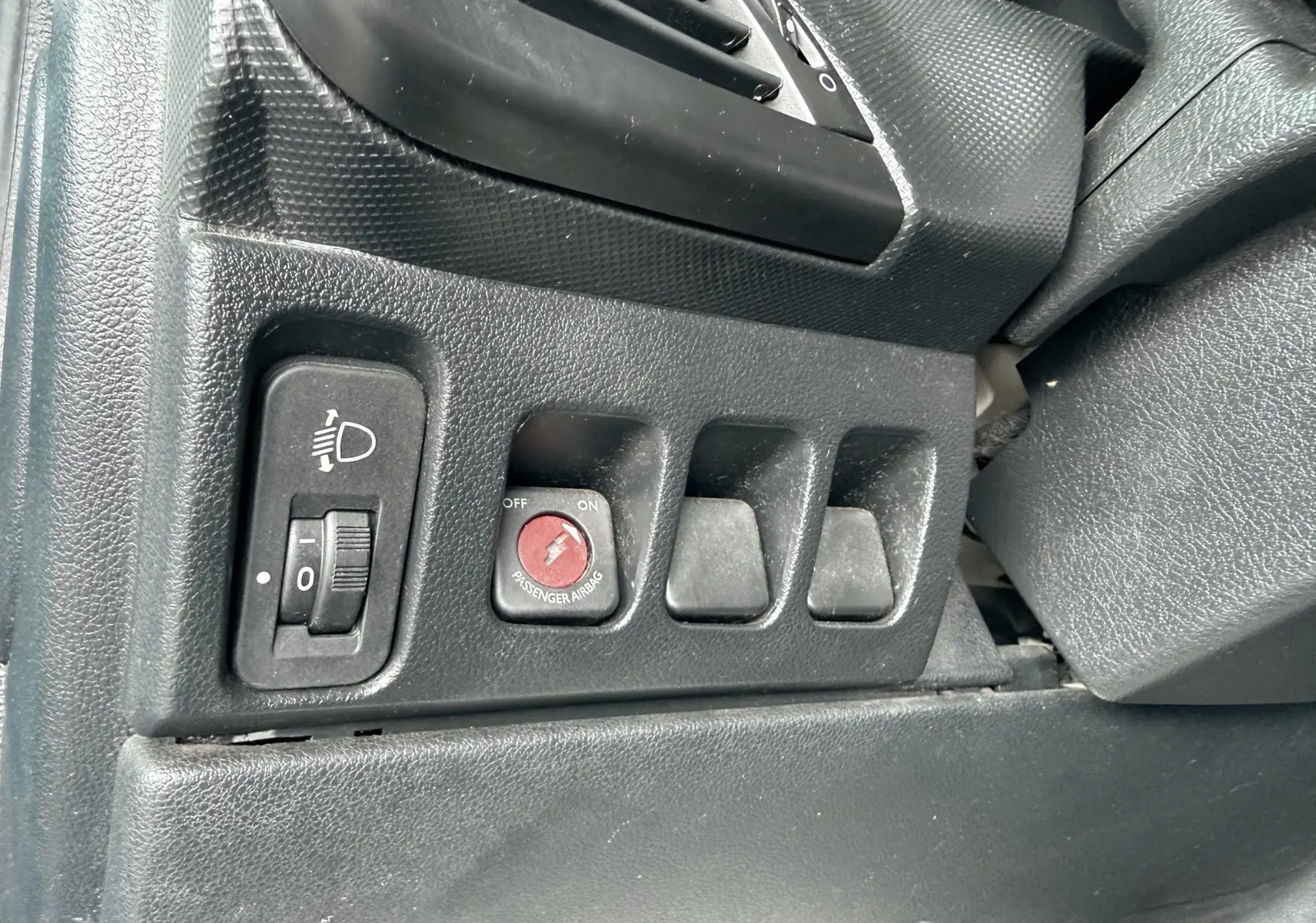 Gros plan sur les commandes noires du tableau de bord côté gauche de la Peugeot 206+ 1.1 i 60 de 2011.