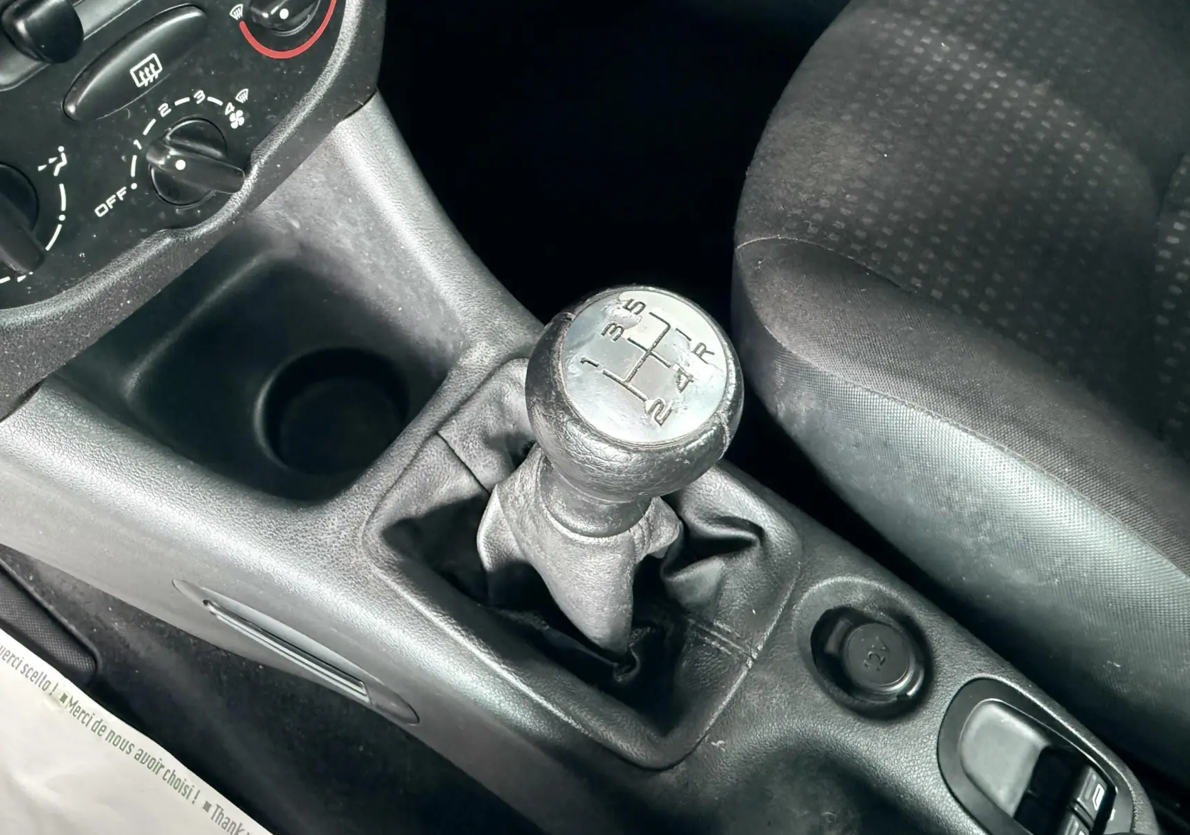 Gros plan sur le levier de vitesses manuel et la console centrale noire de la Peugeot 206+ bleue, côté siège conducteur.