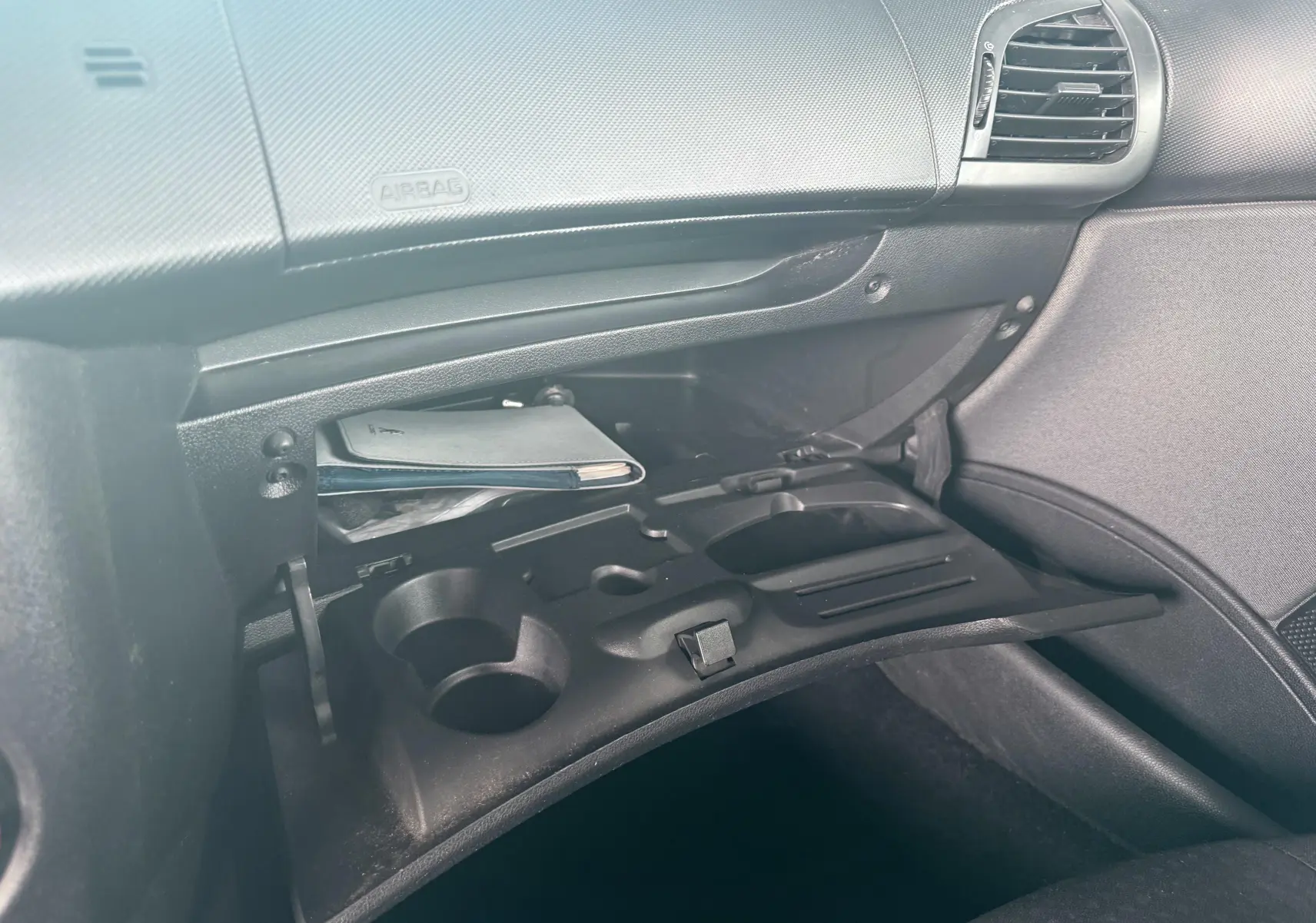 Gros plan sur la boîte à gants ouverte côté passager de la Peugeot 206+ 1.1 i 60 avec intérieur noir.