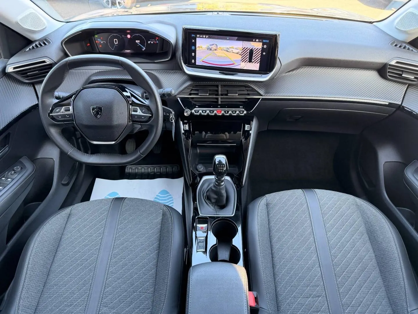 Vue intérieure frontale du poste de conduite du Peugeot 208 1.2 100ch gris Artense avec volant compact et écran tactile central.