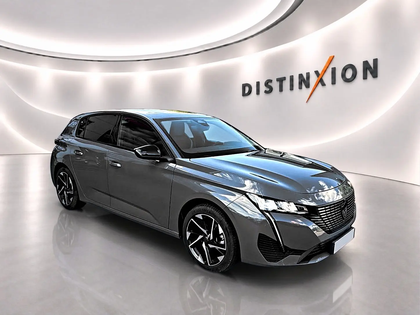 Peugeot 308 gris selenium vue 3/4 avant droit dans un showroom lumineux avec jantes alu noires et logo Distinxion.