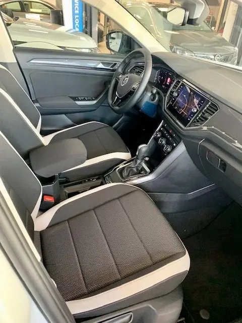Vue intérieure côté conducteur du Volkswagen T-Roc 2021, sièges noir et beige, tableau de bord avec écran tactile et volant multifonction.