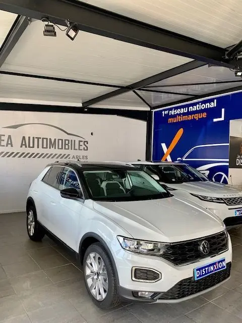 Volkswagen T-Roc blanc vue 3/4 avant droit en intérieur, avec calandre noire et jantes argentées visibles.