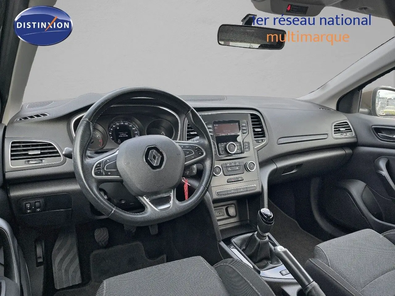 Vue intérieure avant de la Renault Mégane IV TCe 100 Life, tableau de bord et volant noirs avec levier de vitesse manuel.