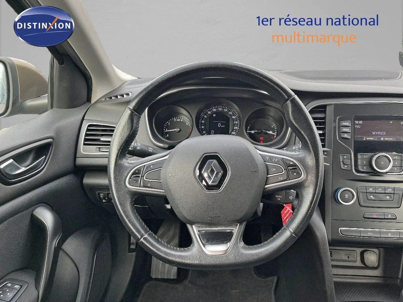 Vue intérieure centrée sur le volant noir d’une Renault Mégane IV brun capuccino, avec tableau de bord et console centrale visibles.