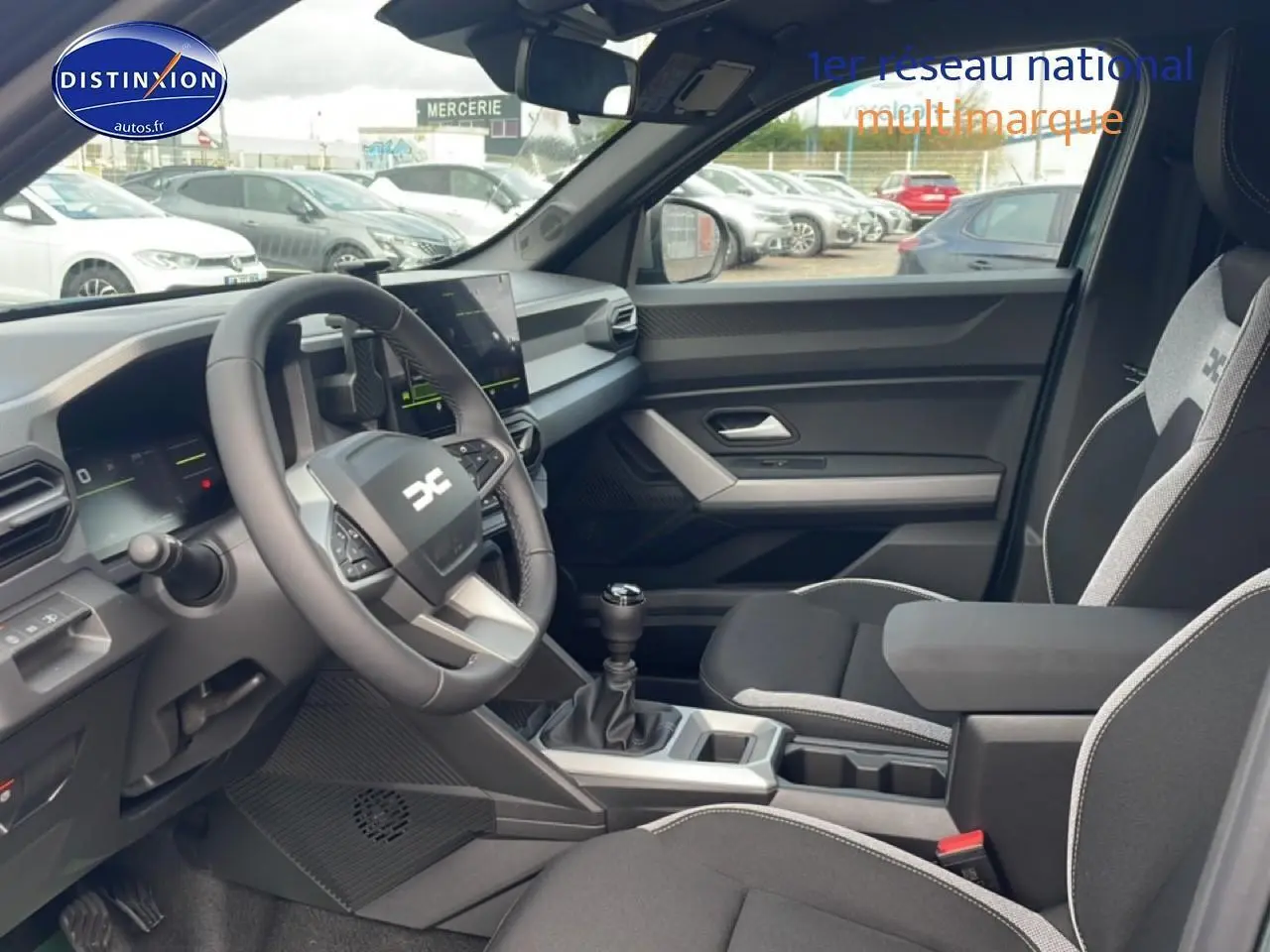 Vue intérieure côté conducteur du Dacia Duster 2026, montrant le volant multifonction, la boîte manuelle et les sièges noirs avec surpiqûres grises.