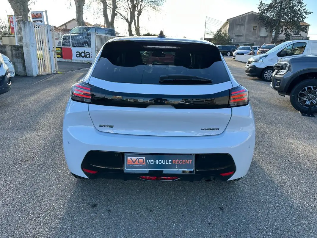 Vue arrière d'une Peugeot 208 Hybrid blanche de 2025 avec feux LED et bande noire distinctive sur le coffre.
