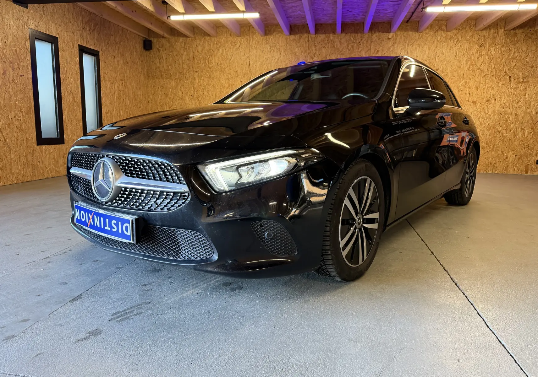 Vue 3/4 avant droit d'une Mercedes Classe A noire avec calandre étoilée et jantes alliage dans un garage en bois.