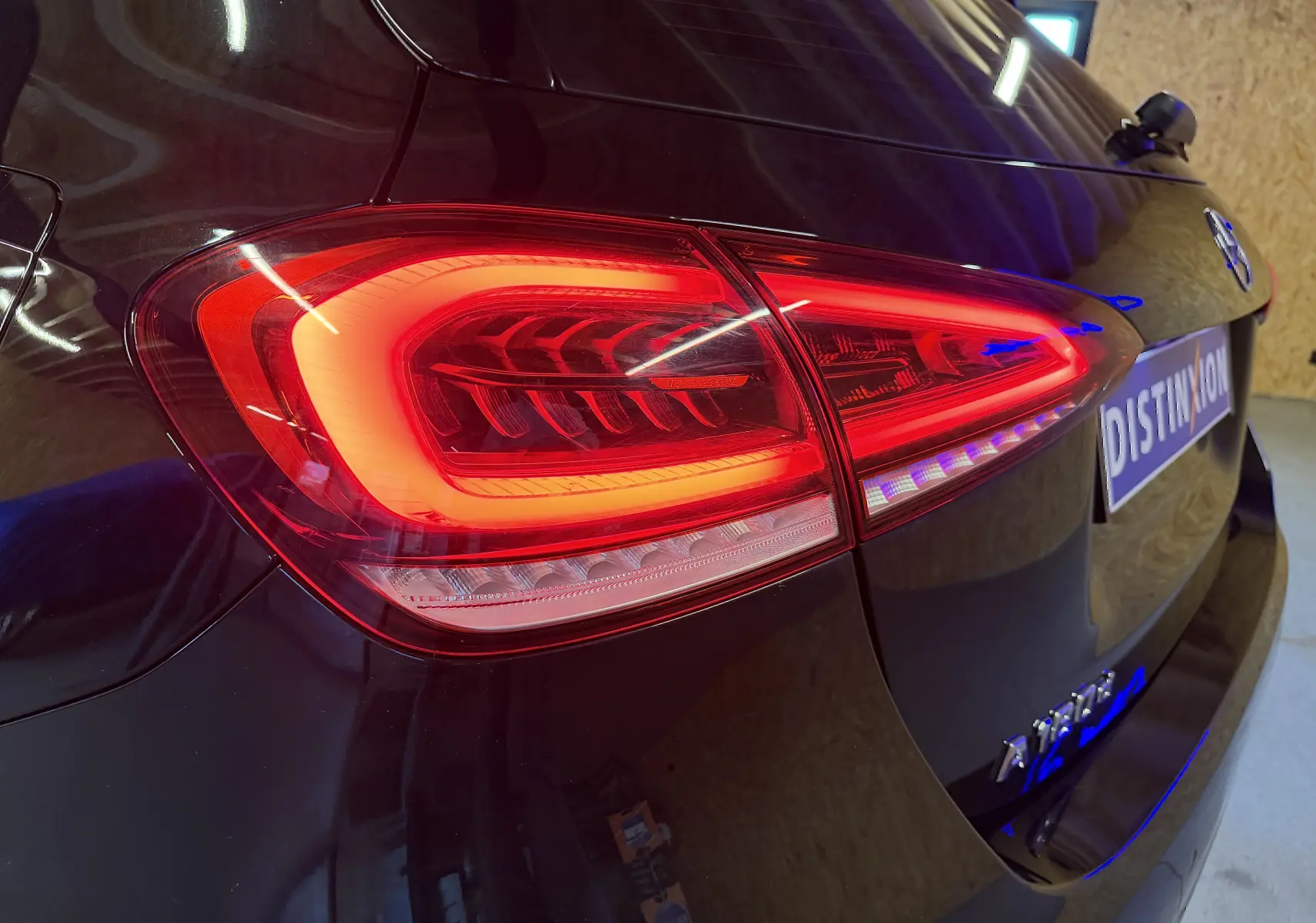 Gros plan sur le feu arrière gauche rouge d'une Mercedes Classe A noire, avec reflet lumineux sur la carrosserie.