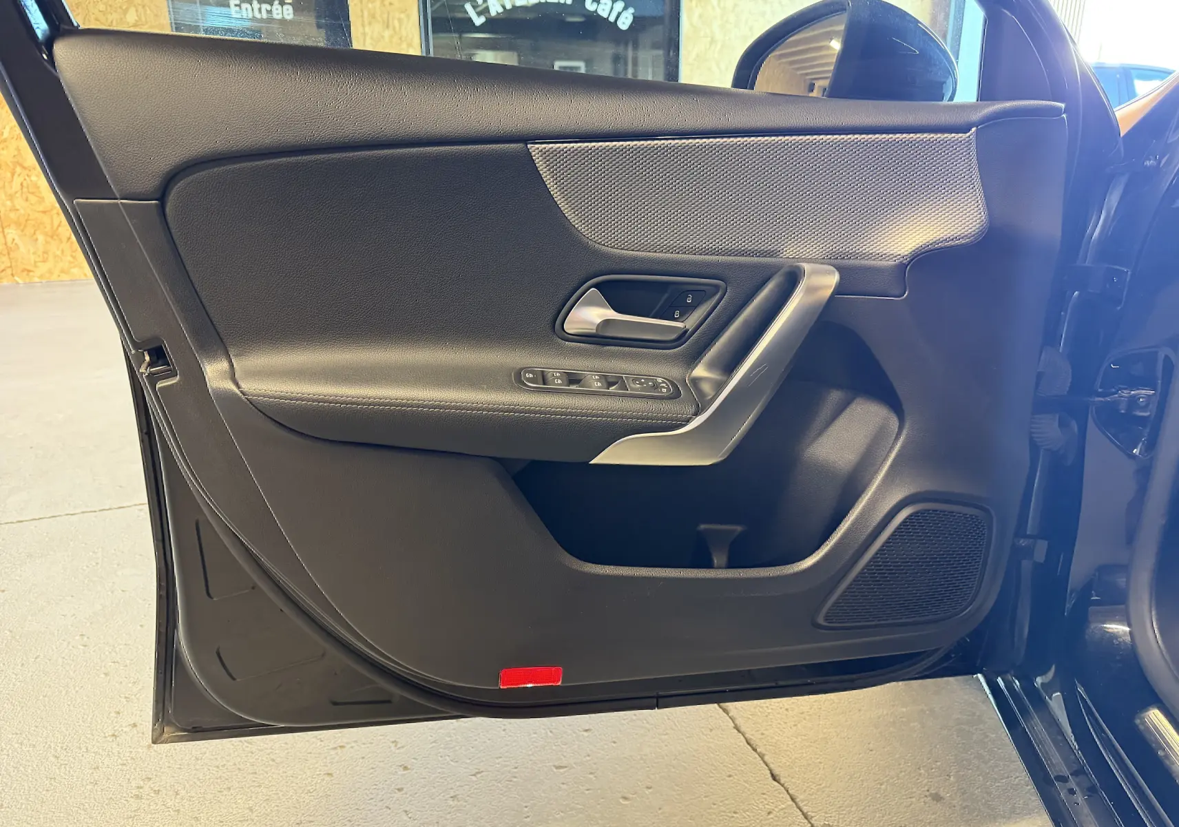 Vue intérieure du panneau de porte avant gauche noir de la Mercedes Classe A 2022 avec commandes électriques et haut-parleur intégré.