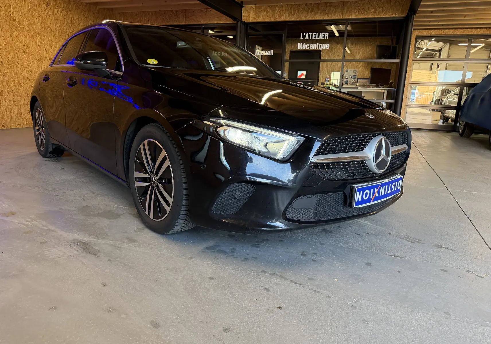Mercedes Classe A noire vue en 3/4 avant droit dans un garage, avec jantes alu et calandre étoilée distinctive.