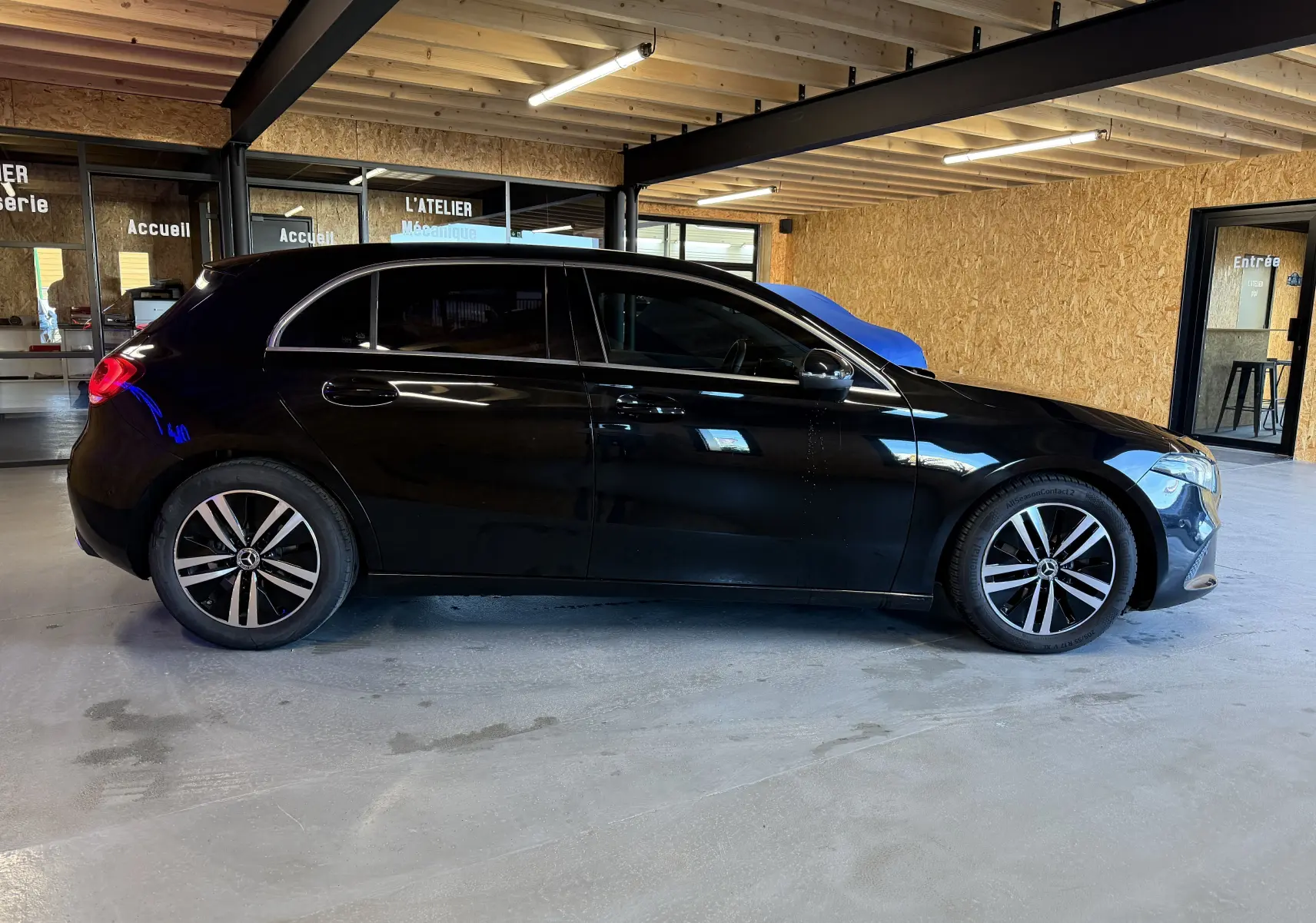 Vue latérale droite d'une Mercedes Classe A noire avec jantes alliage, stationnée en intérieur dans un atelier.