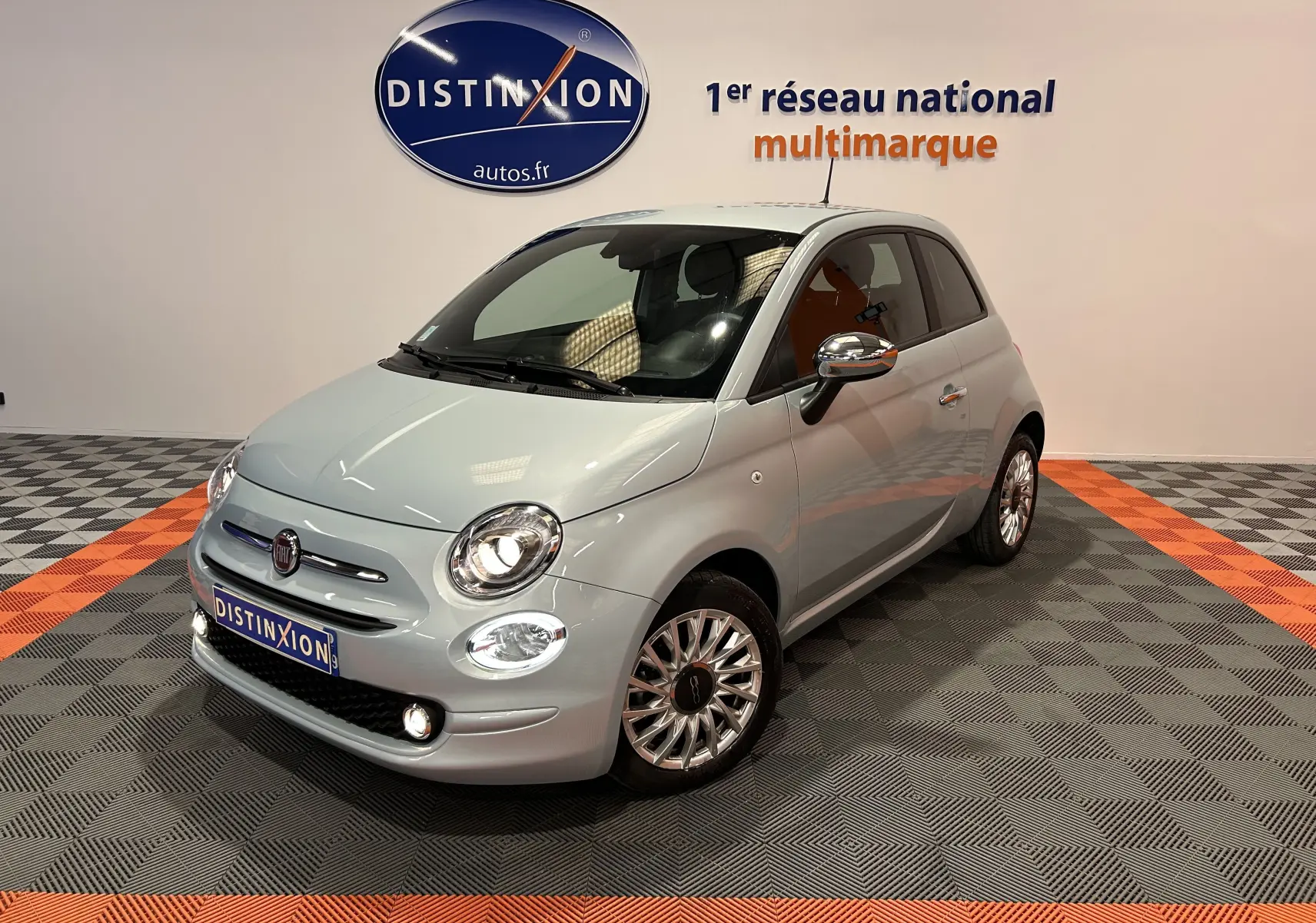 Vue 3/4 avant d'une Fiat 500 gris clair avec jantes alliage et rétroviseurs chromés en showroom.