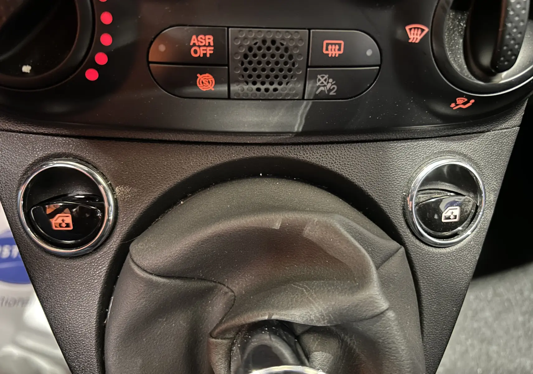 Gros plan sur la console centrale de la Fiat 500 2023, montrant le levier de vitesses manuel et les commandes des vitres électriques.