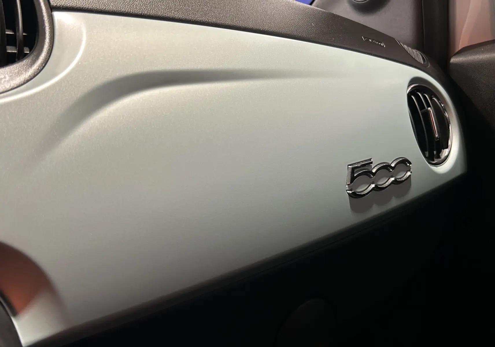 Vue rapprochée de la planche de bord Rugiada Green de la Fiat 500 avec logo 500 chromé et sortie d’air ronde.