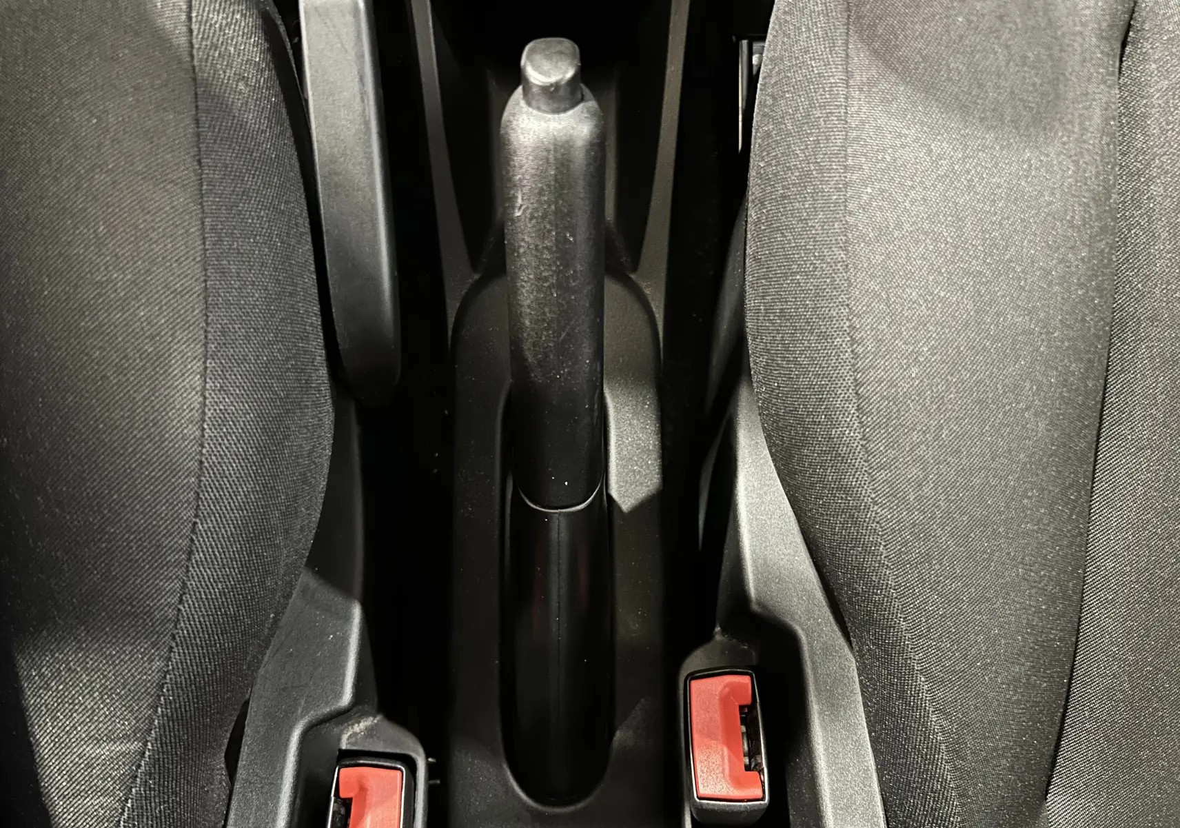 Vue plongeante sur le frein à main et les ceintures de sécurité entre les sièges avant en tissu gris de la Fiat 500.