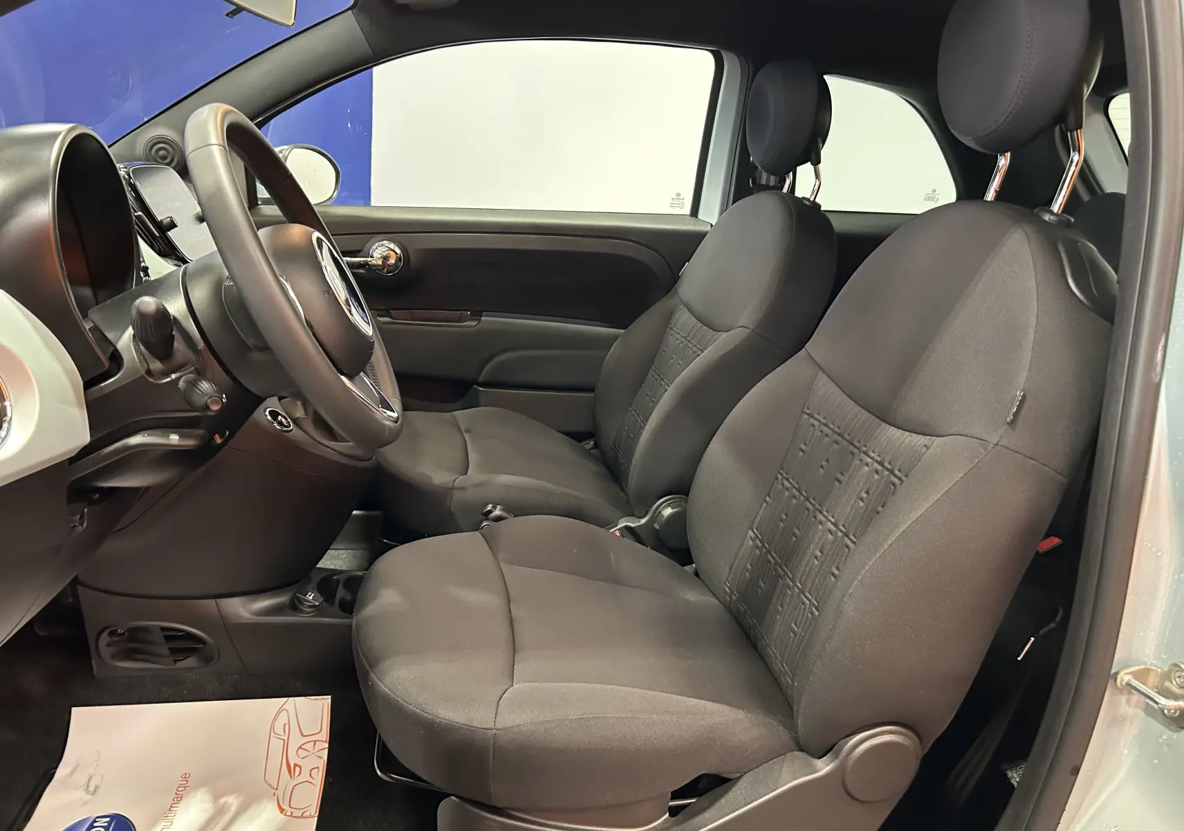 Vue intérieure côté conducteur de la Fiat 500 2023 Rugiada Green, sièges tissu noir et tableau de bord compact.