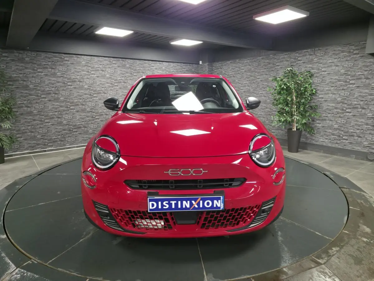 Vue avant d'une FIAT 600 rouge brillante avec logo 600 et plaque Distinxion en intérieur showroom.