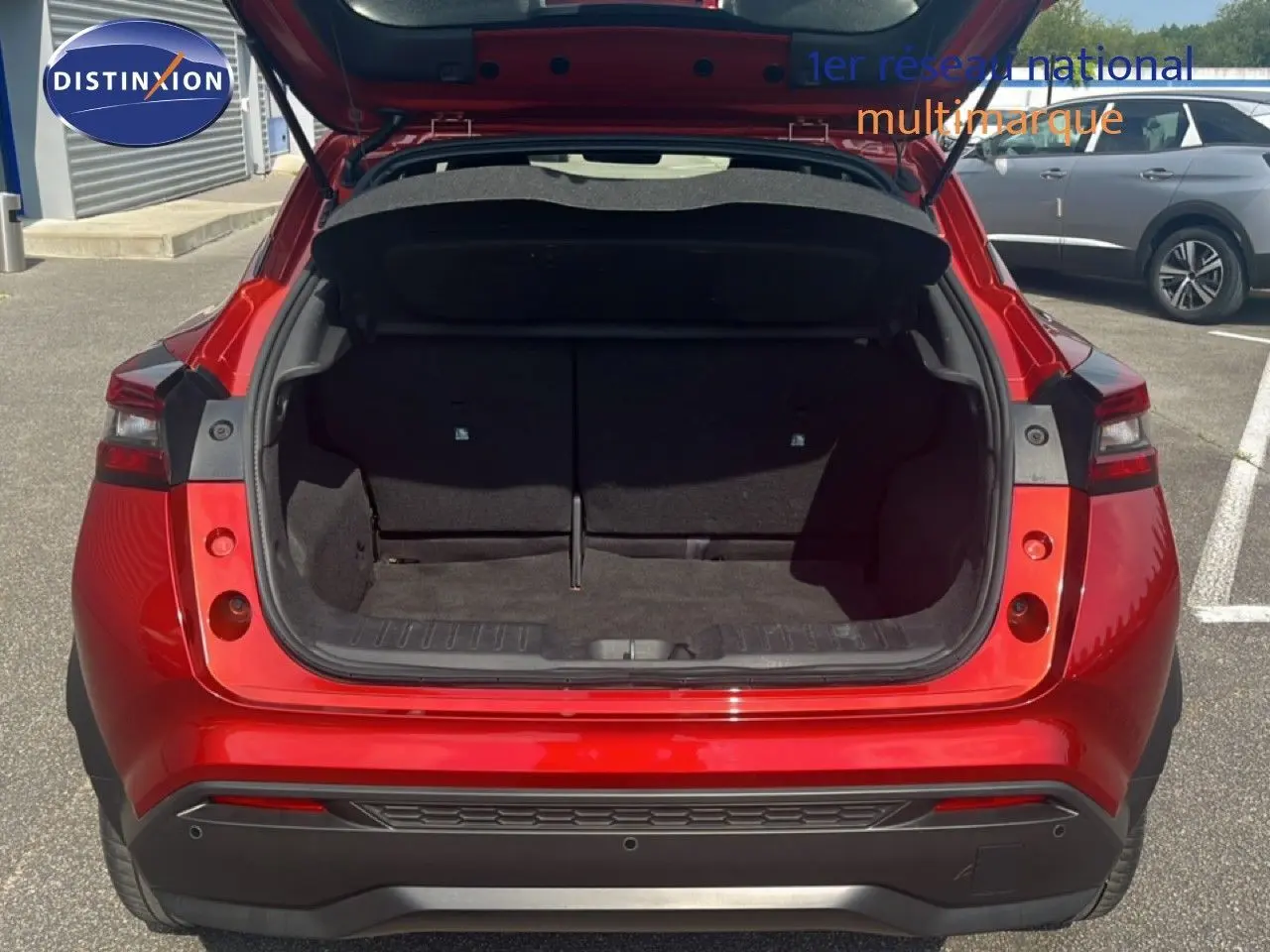 Vue arrière avec coffre ouvert du Nissan Juke 2024 rouge Fuji Metal, soulignant son espace de chargement généreux.