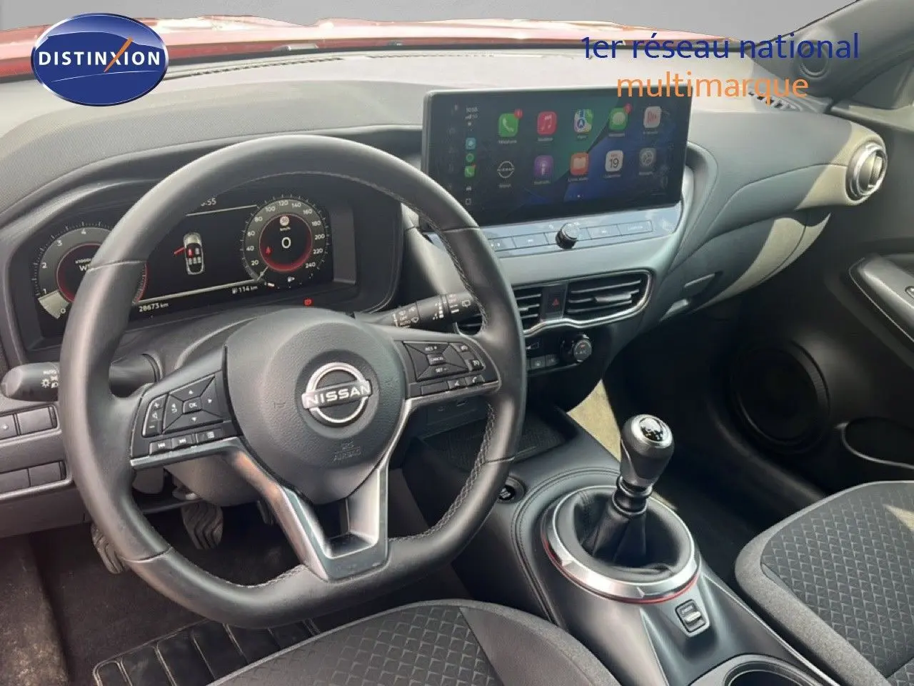 Vue intérieure du poste de conduite du Nissan Juke 2024, volant cuir et levier de vitesse manuelle visibles.