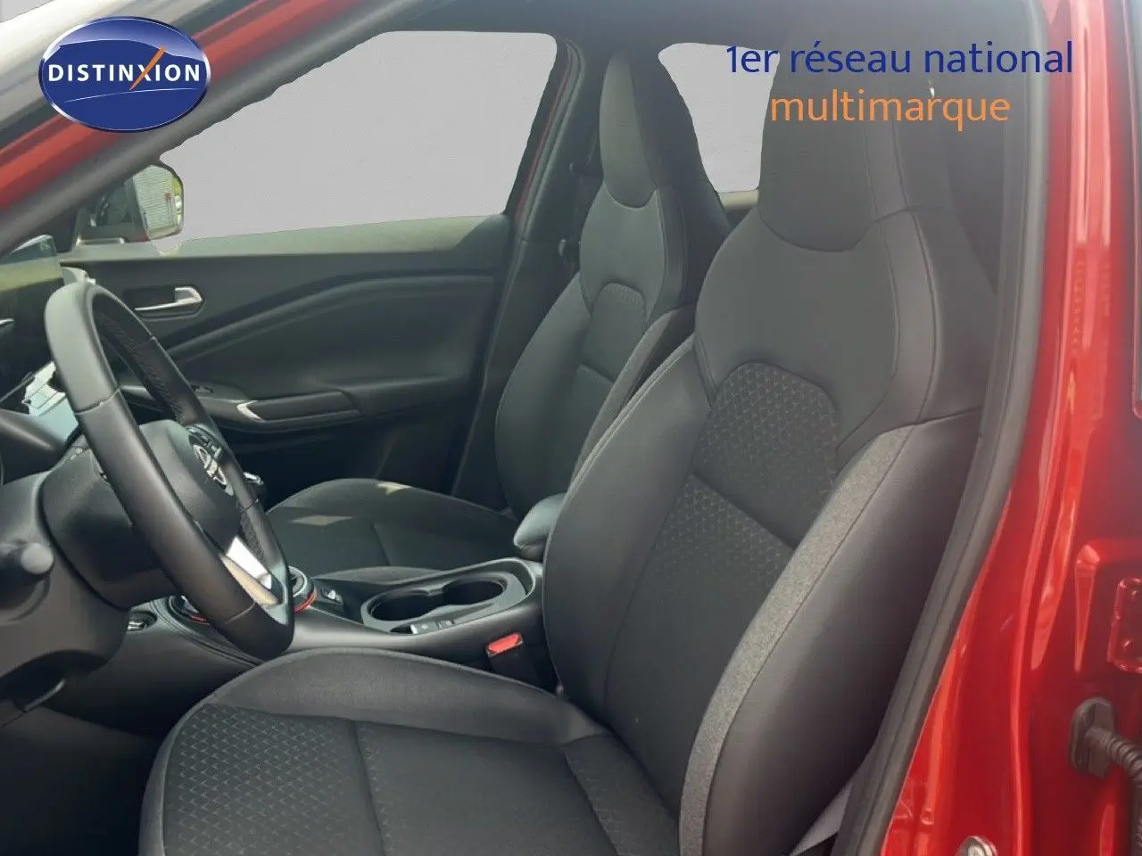 Vue intérieure côté conducteur du Nissan Juke rouge Fuji Metal 2024, sièges noirs en tissu et cuir avec volant multifonction.