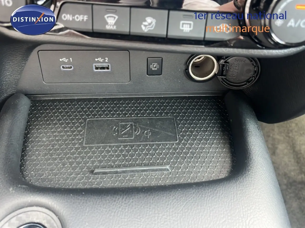 Détail de la console centrale du Nissan Juke 2024 rouge Fuji Metal, montrant les ports USB, prise 12V et zone de recharge sans fil.