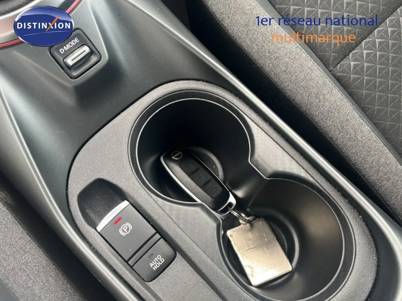 Vue rapprochée de la console centrale noire du Nissan Juke 2024 avec clé dans porte-gobelet et bouton frein à main électrique.