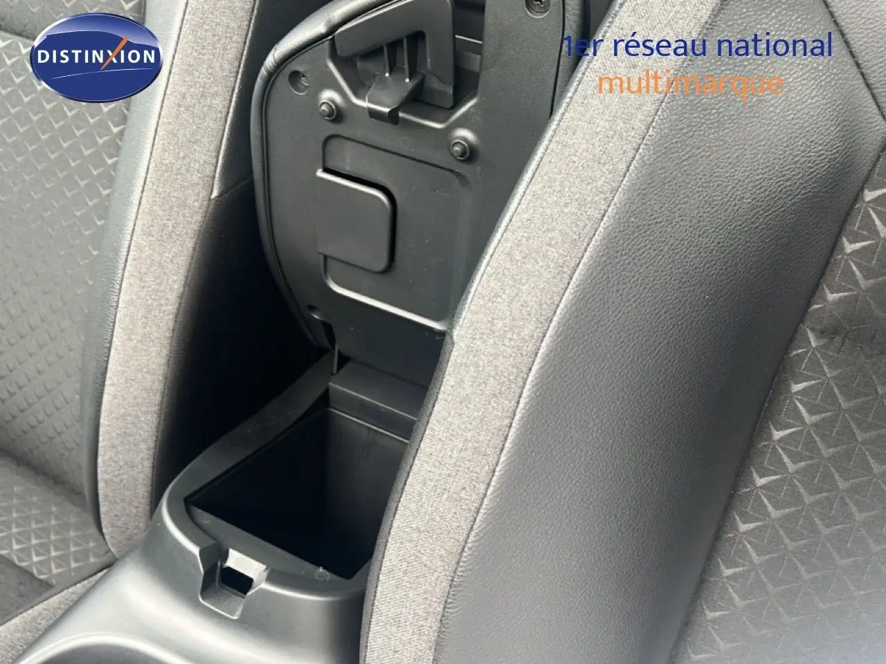 Gros plan sur la console centrale ouverte entre les sièges avant en tissu gris et simili cuir noir du Nissan Juke 2024.