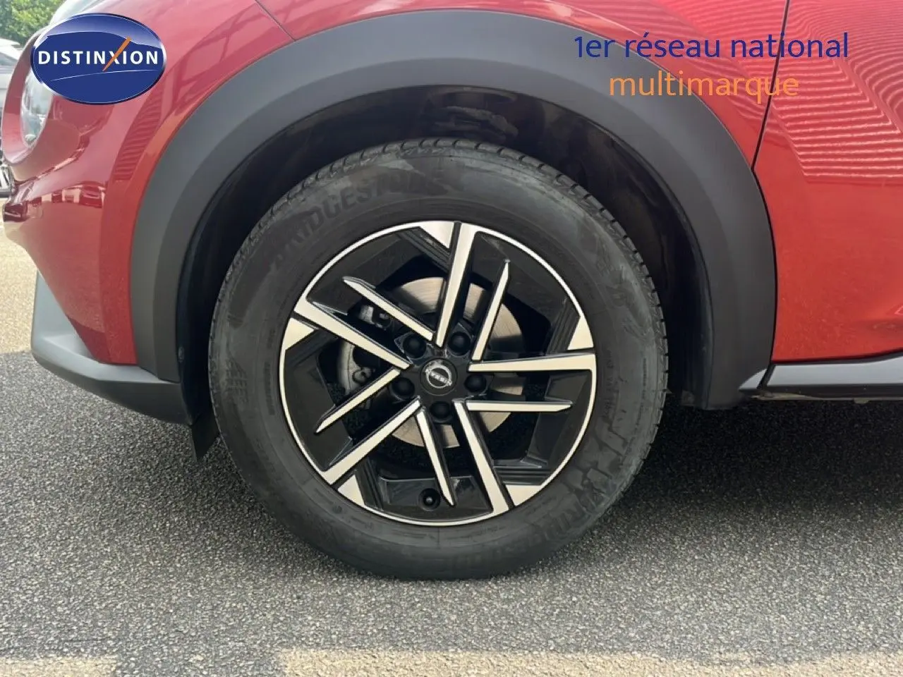 Gros plan sur la roue avant droite du Nissan Juke rouge Fuji Metal 2024 avec jante alliage noire et argent.