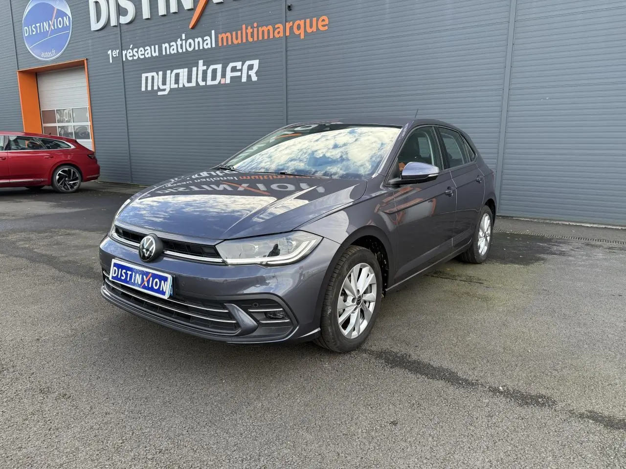Volkswagen Polo gris cendre vue 3/4 avant droit, stationnée devant un mur gris avec logo Distinxion.