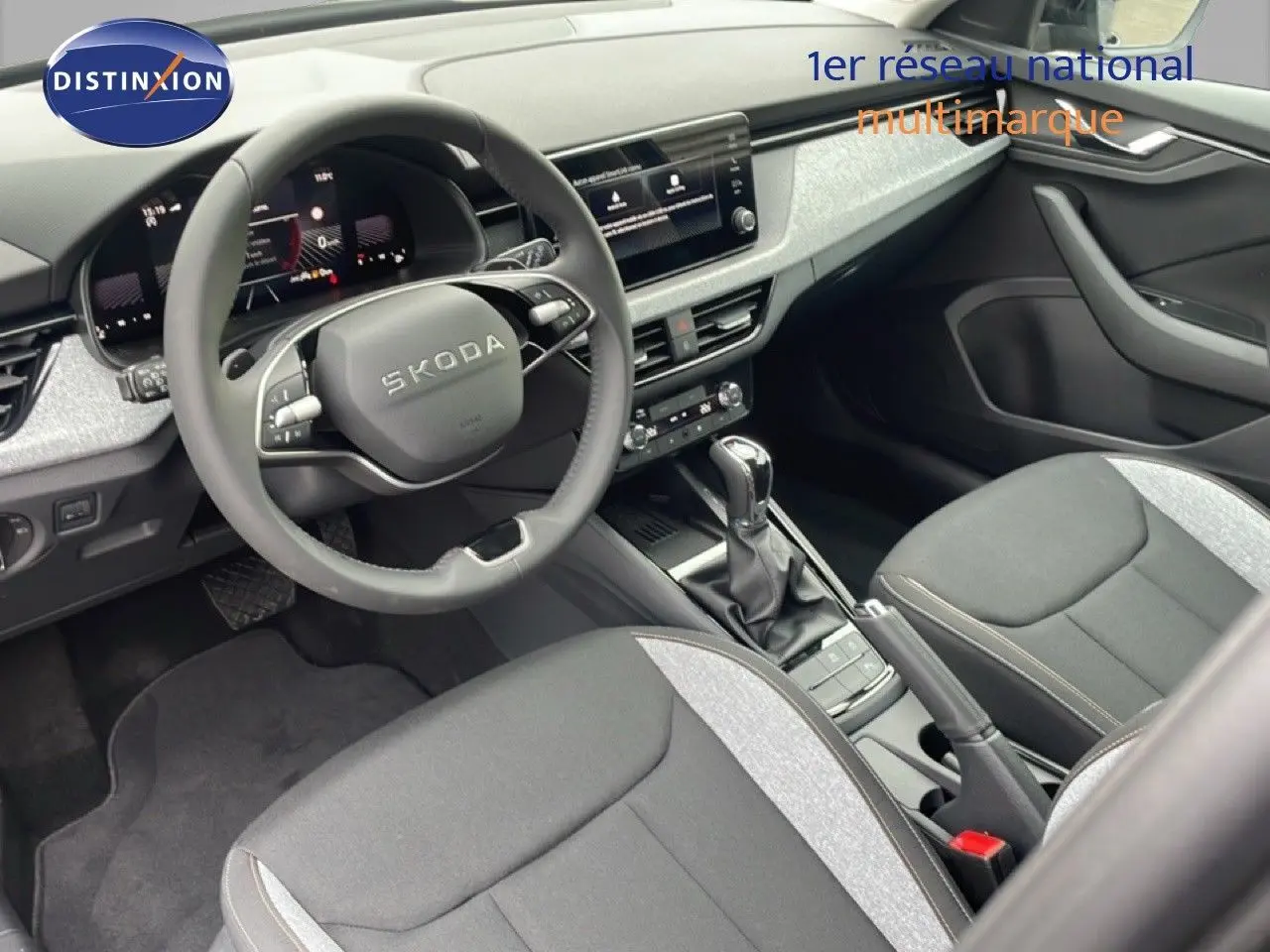 Intérieur du Skoda Kamiq 2025 en tissu noir et gris, vue côté conducteur sur le tableau de bord et la console centrale.