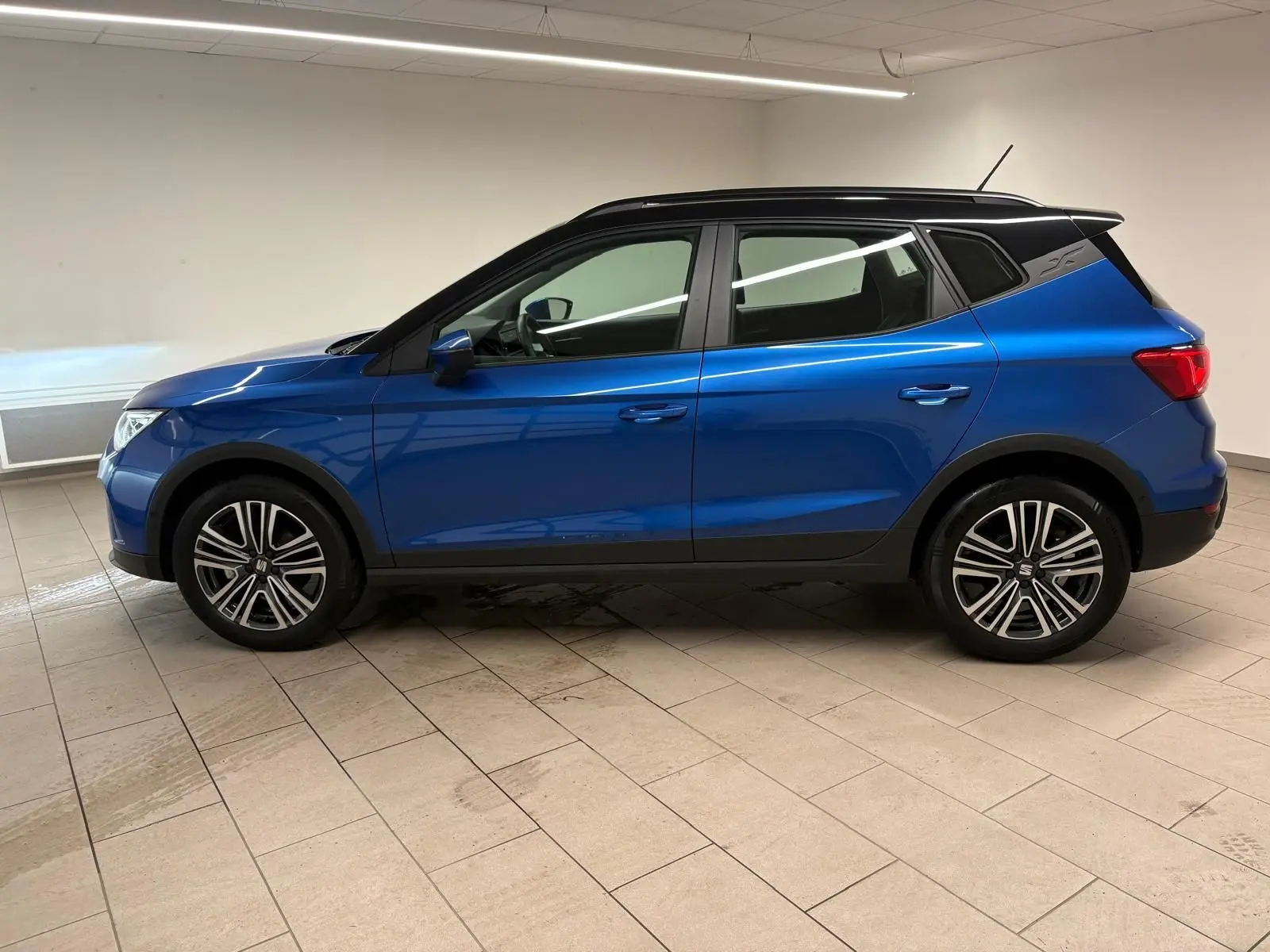Vue de profil côté gauche du SEAT Arona 2025 en bleu saphir avec toit noir, soulignant ses jantes et lignes modernes.