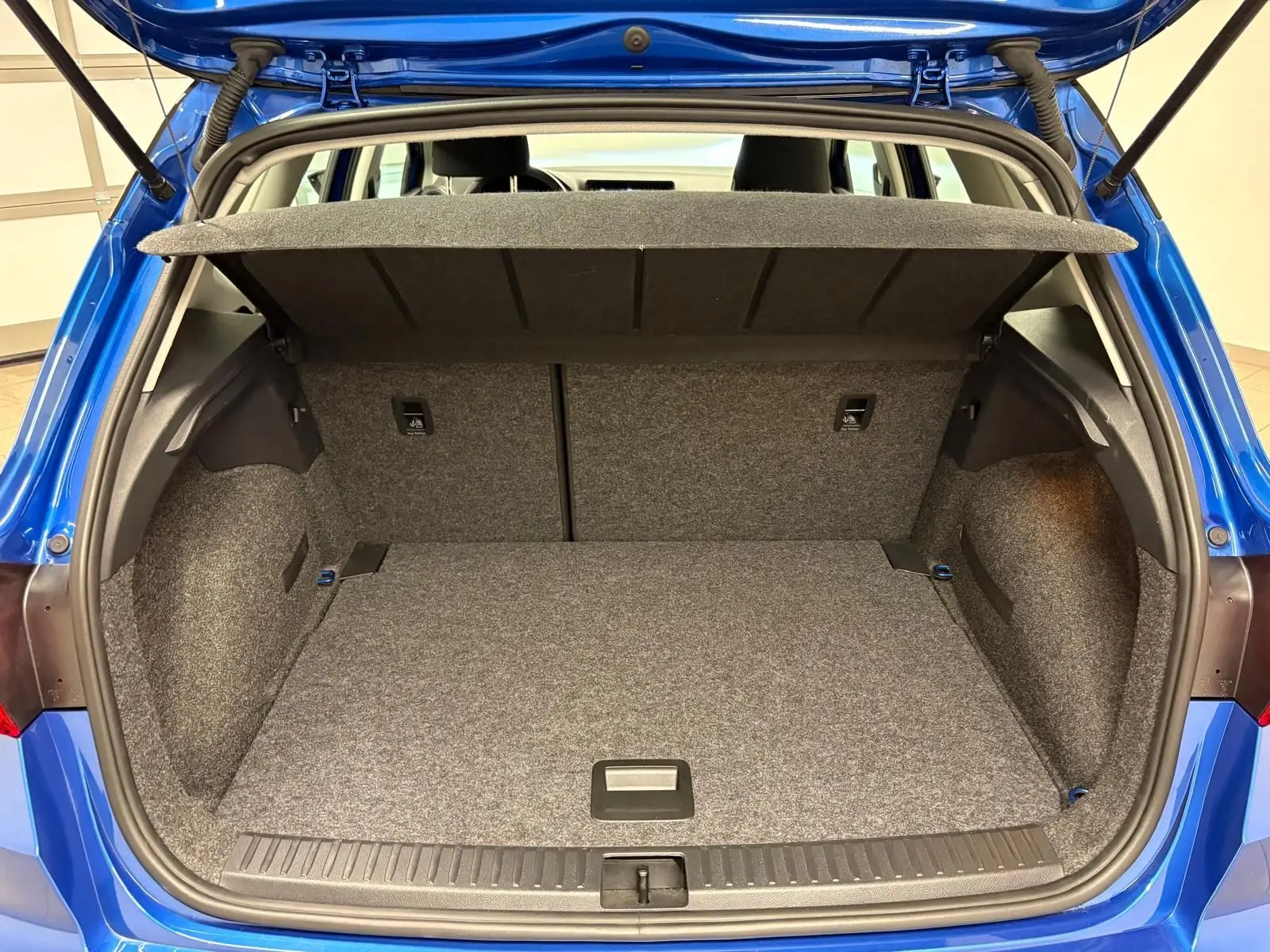 Coffre ouvert d’un SEAT Arona Bleu Saphir, vue arrière montrant l’espace de chargement vide et la tablette cache-bagages relevée.