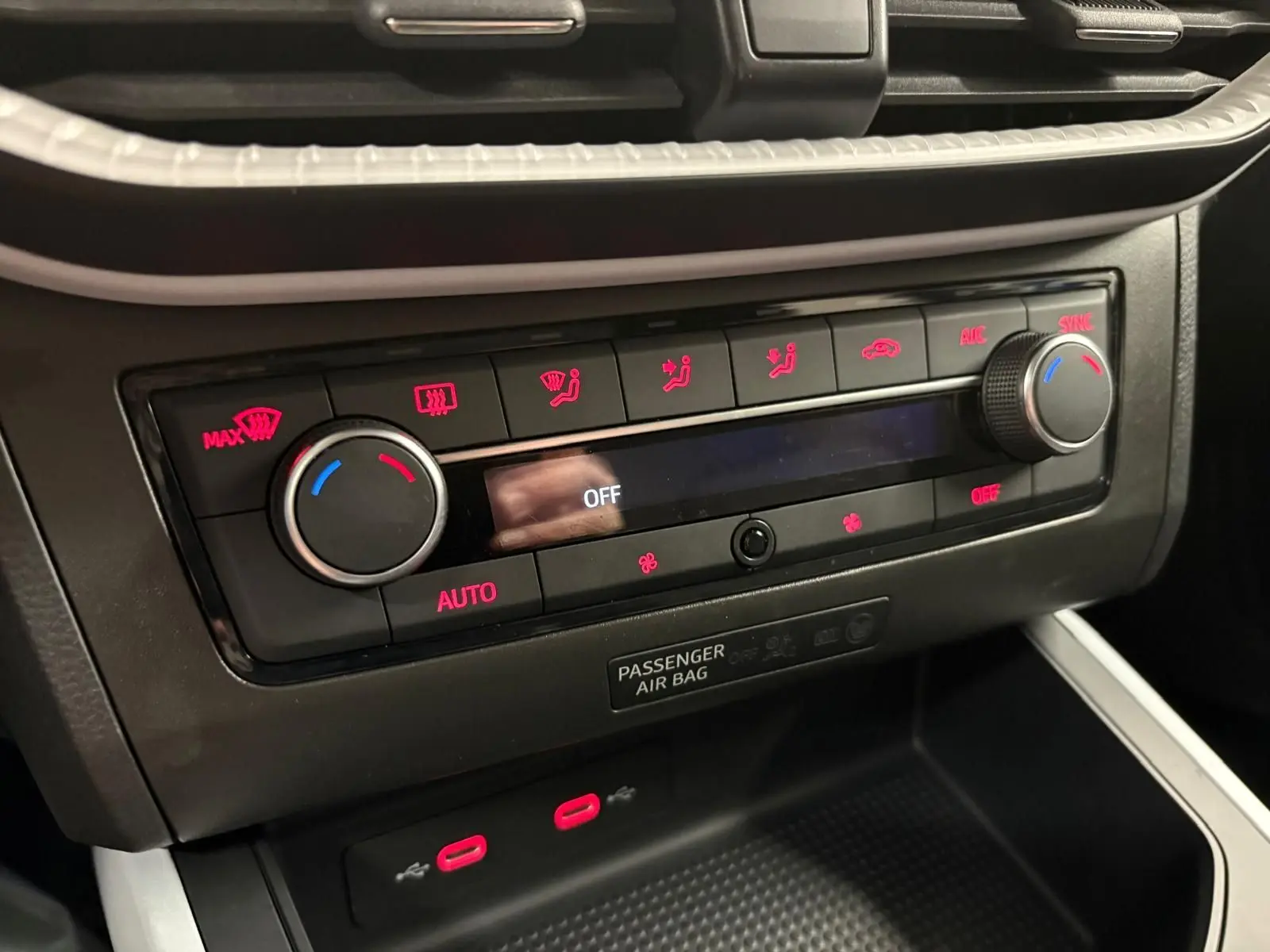 Gros plan sur la console centrale du SEAT Arona 2025, montrant les commandes de climatisation avec éclairage rouge.