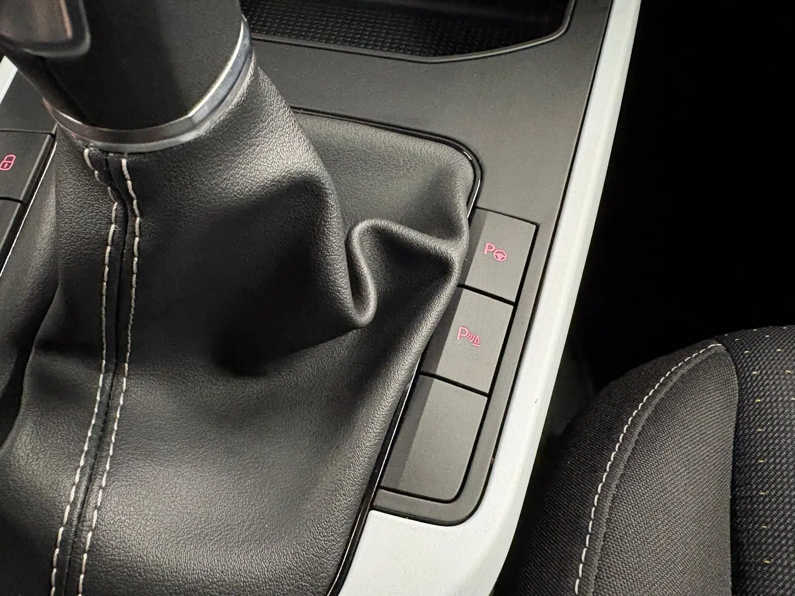 Gros plan sur la console centrale du SEAT Arona 2025, montrant le soufflet de levier de vitesses noir et les boutons de stationnement assisté.
