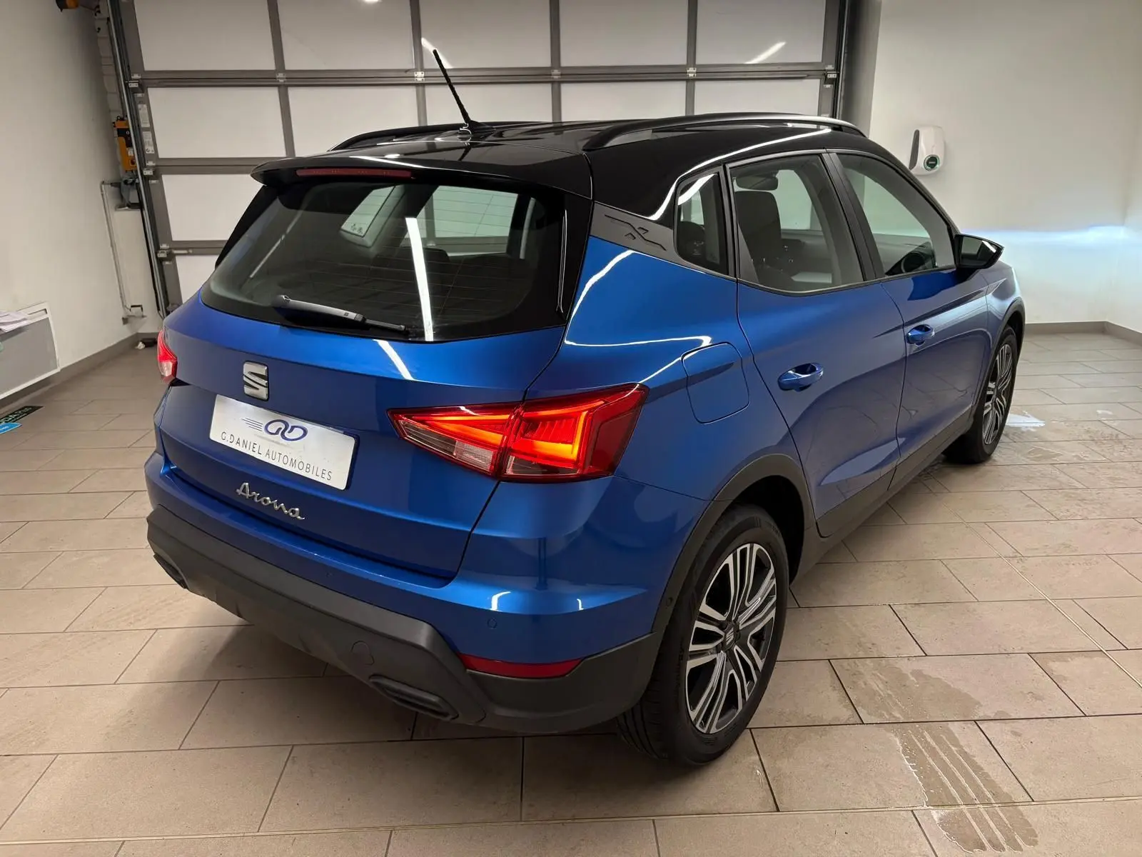 Vue 3/4 arrière droite d'un SEAT Arona bleu saphir avec toit noir, feux arrière allumés en intérieur.