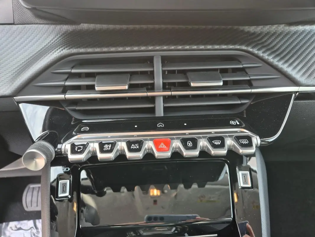 Vue rapprochée du tableau de bord noir brillant de la Peugeot 208 Hybrid 110 e-DCS6 Allure avec commandes climatisation et boutons fonctionnels.
