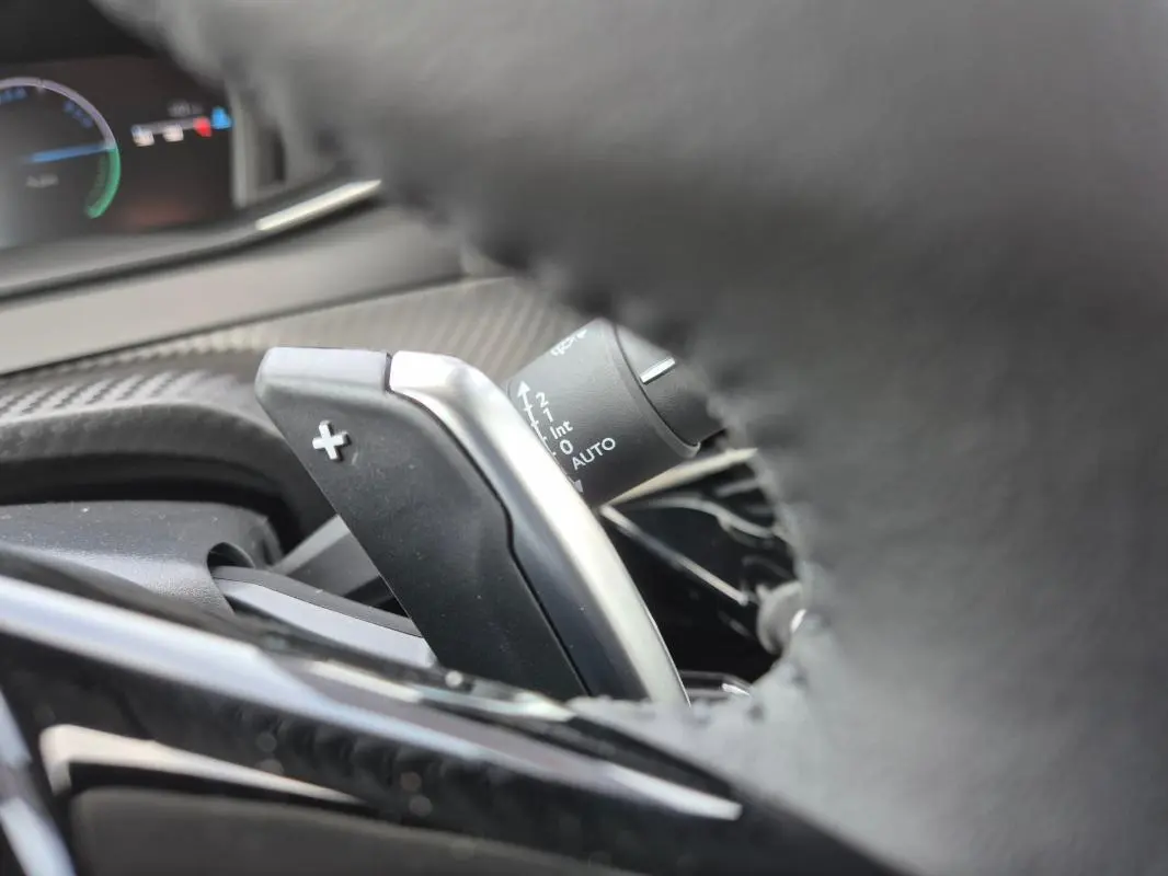 Gros plan sur la palette de changement de vitesse droite du volant d’une Peugeot 208 Hybrid blanche, tableau de bord en arrière-plan.