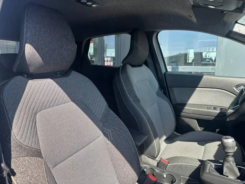 Vue intérieure côté avant droit du Renault Captur 2025, sièges tissu gris avec surpiqûres contrastées et levier de vitesse manuel.