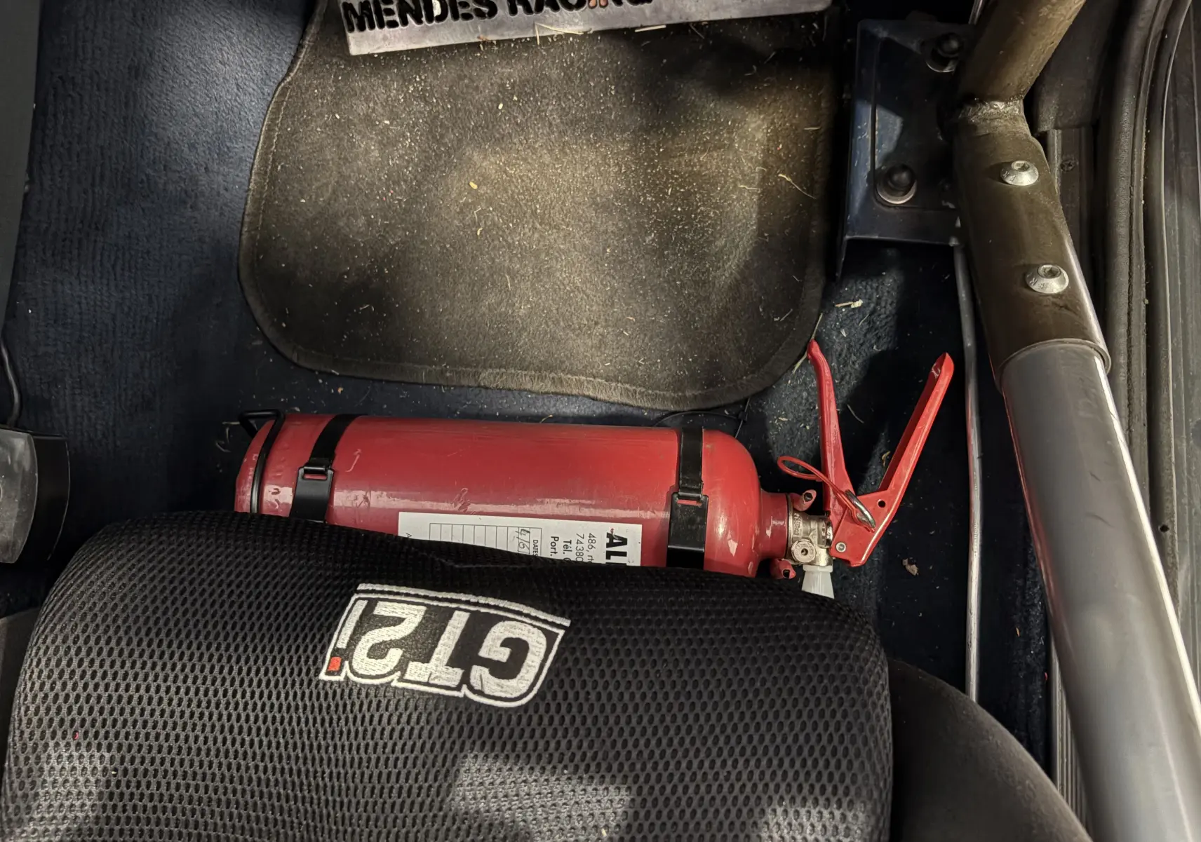 Extincteur rouge fixé au sol côté droit d'un Audi Coupé GT 1983 avec siège GT2i noir et arceau de sécurité.