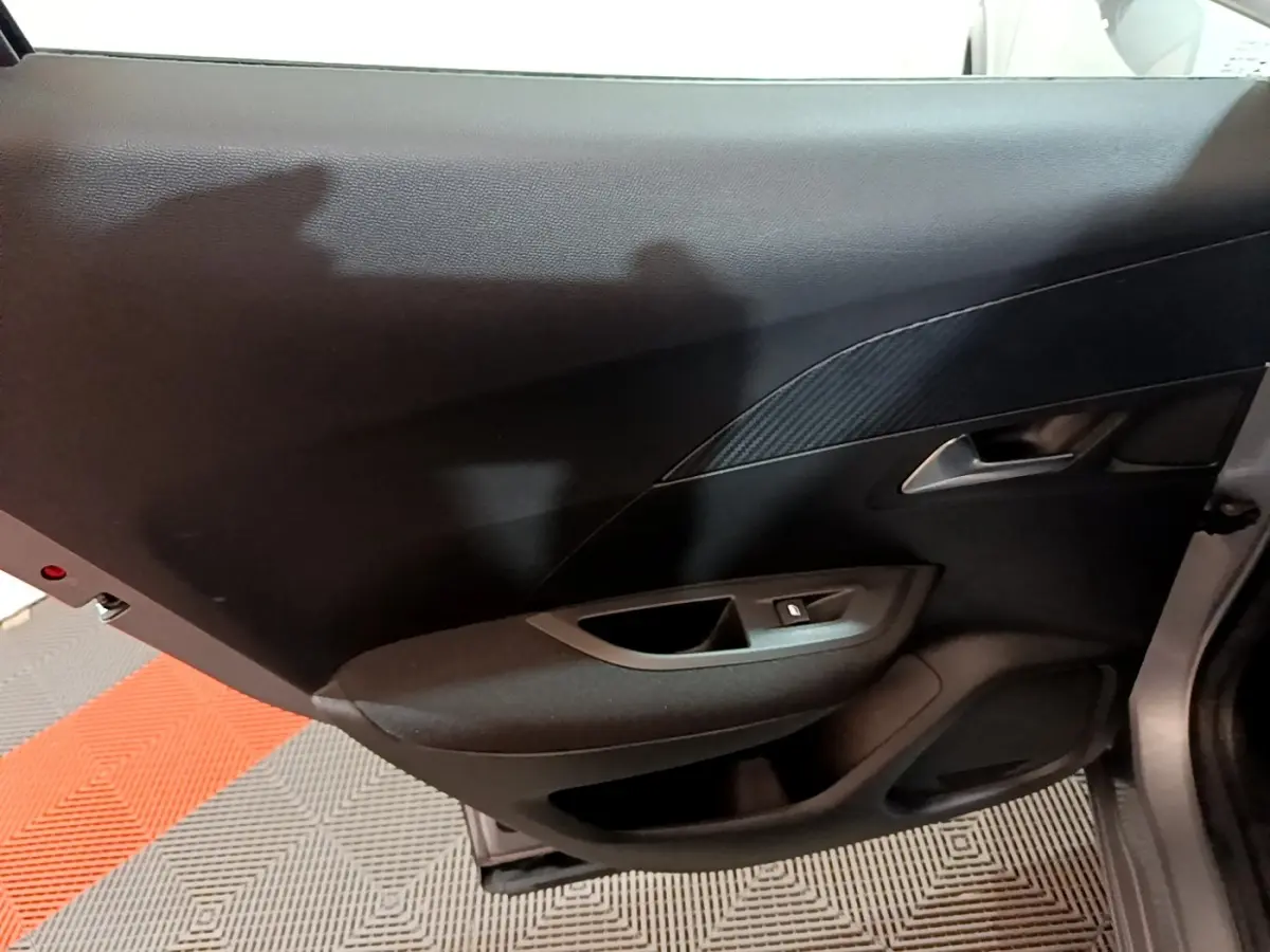 Vue intérieure du panneau de porte arrière gauche gris foncé du Peugeot 2008 avec poignée argentée et commande de vitre.