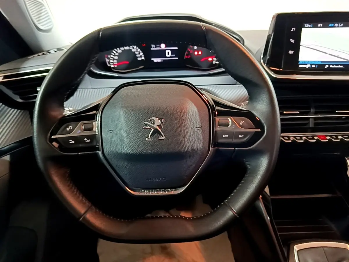 Vue rapprochée du volant cuir noir de la Peugeot 2008 2021 avec tableau de bord numérique et écran tactile central.