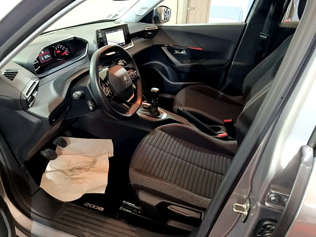 Vue intérieure côté conducteur du Peugeot 2008 gris clair, avec volant cuir, tableau de bord numérique et sièges tissu noirs.