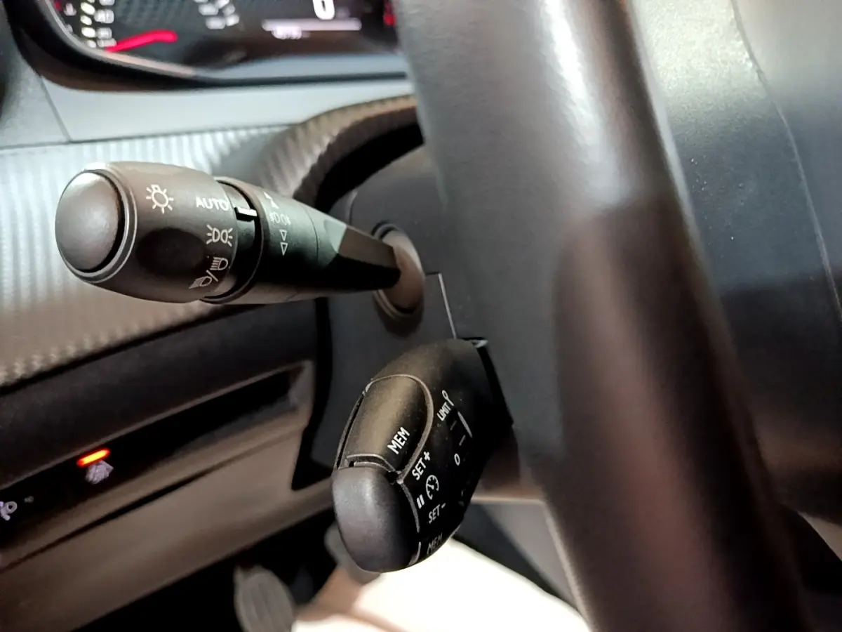 Gros plan sur les commandes au volant du Peugeot 2008 gris clair, montrant les leviers de clignotants et régulateur de vitesse.