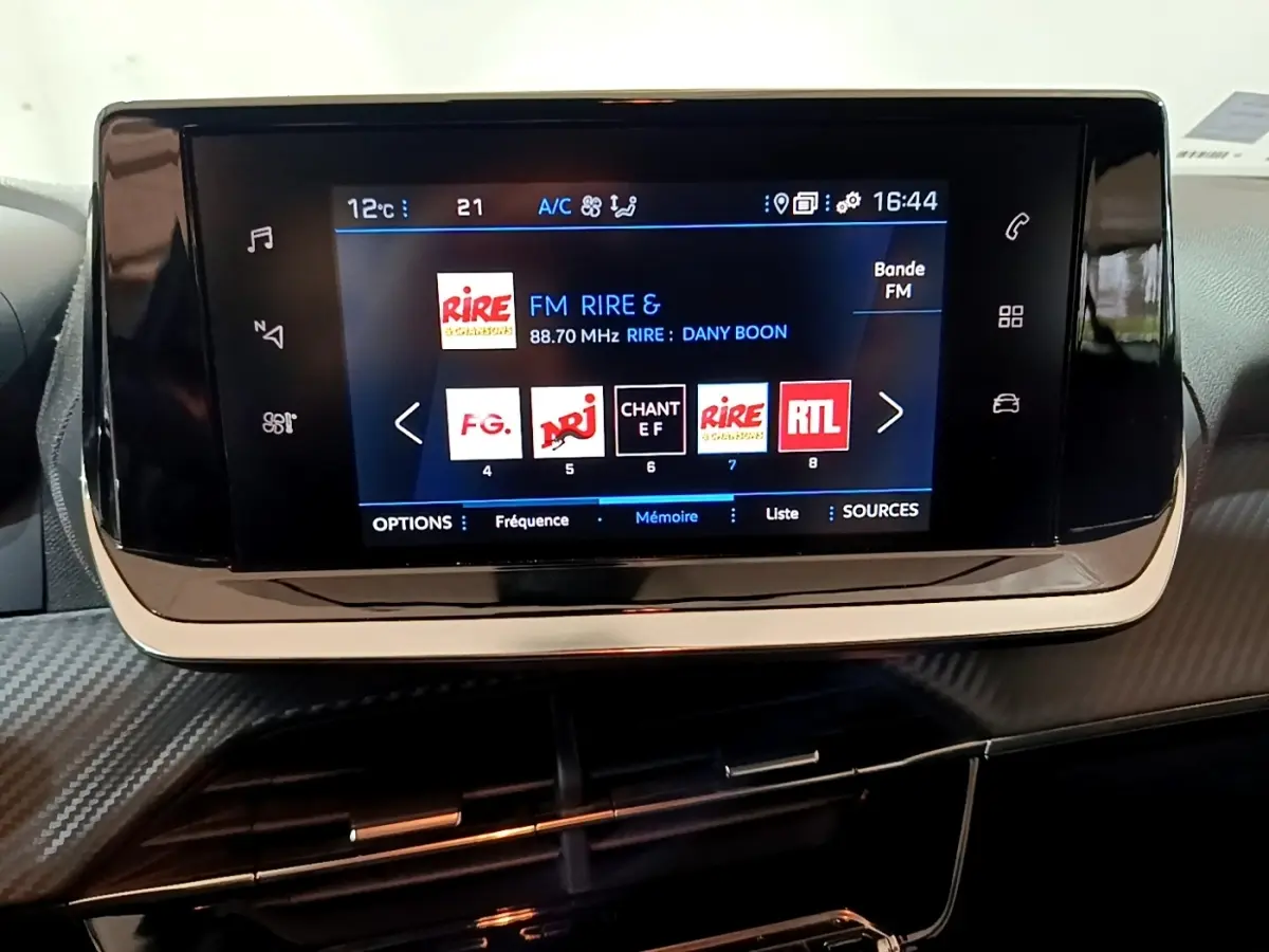 Écran tactile central du tableau de bord de la Peugeot 2008 gris clair, affichant les stations radio FM.