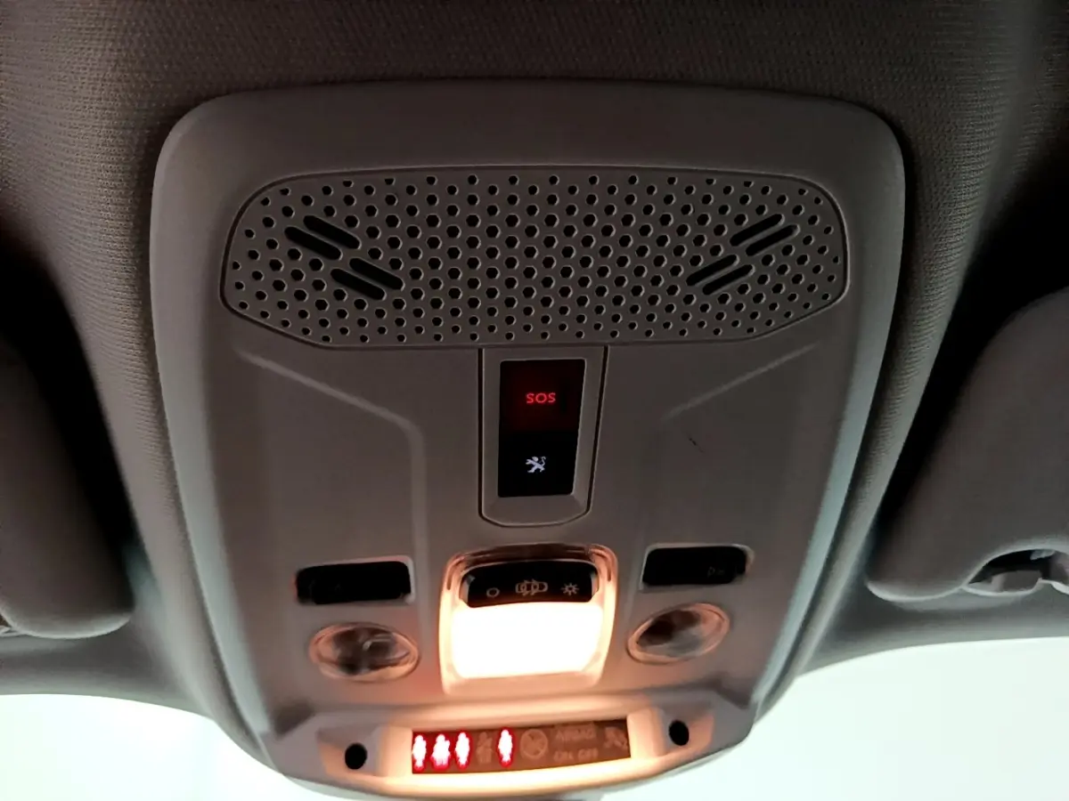 Vue en contre-plongée du plafonnier gris clair du Peugeot 2008 avec bouton SOS et éclairage intérieur allumé.