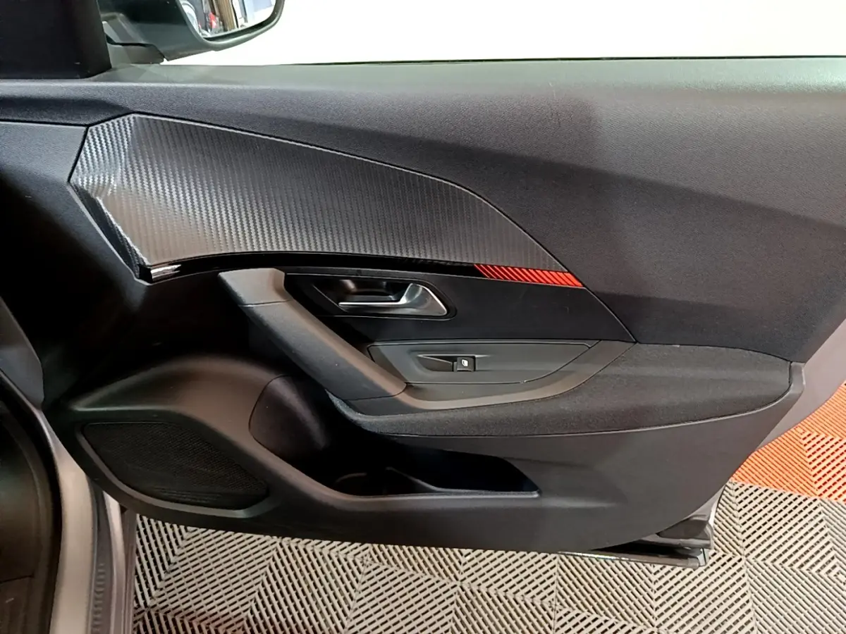 Vue intérieure du panneau de porte avant gauche du Peugeot 2008 gris clair, avec insert imitation carbone et bande rouge décorative.