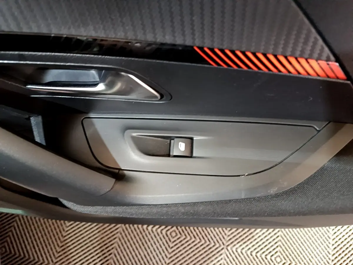 Gros plan sur la commande de lève-vitre côté conducteur avec insert décoratif noir et rouge dans une Peugeot 2008 gris clair.