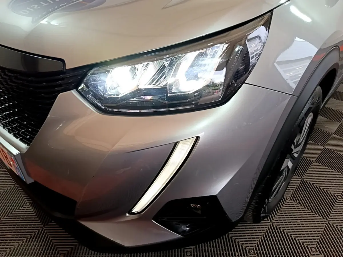 Gros plan sur l'avant droit gris clair du Peugeot 2008 2021 avec phares LED allumés et feux diurnes verticaux.